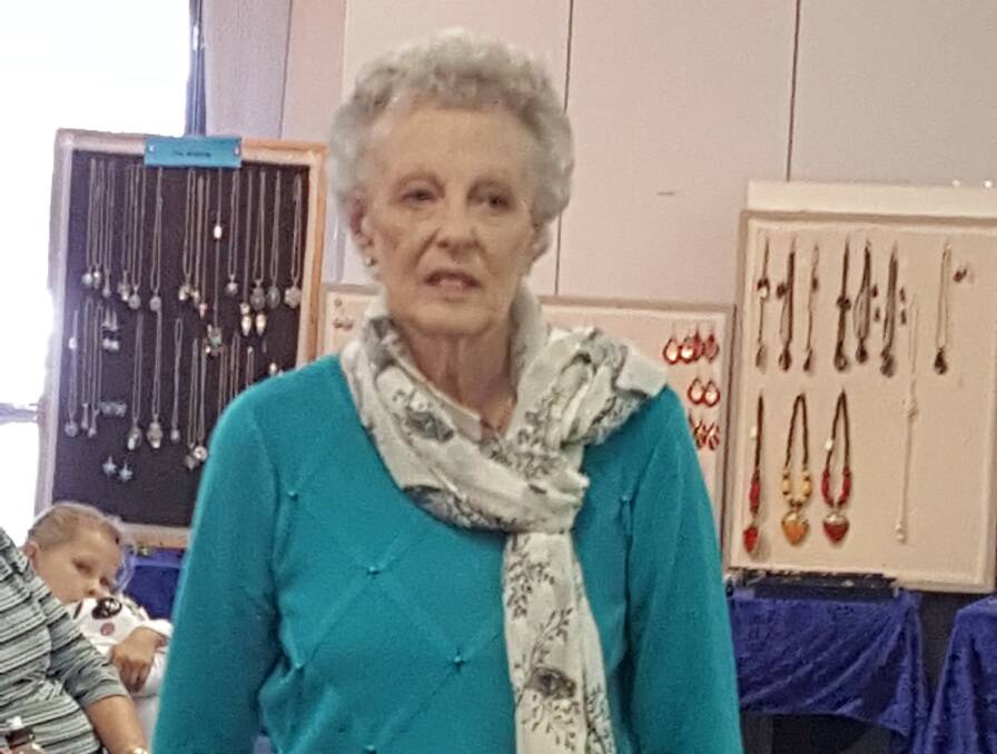 Carole Osborne wearing an aqua jumper featuring a diamond pattern picked out with imitation pearl and a fine patterned scarf over black classic pants.