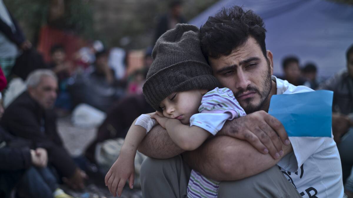 A Syrian refugee child sleeps in his father's arms while waiting at a resting point to board a bus, after arriving on a dinghy from the Turkish coast to the northeastern Greek island of Lesbos. Picture: AP 