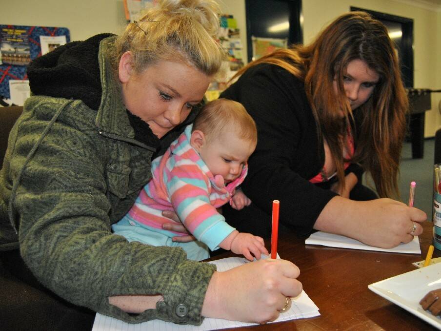 Macy McDonald-Keys  holds Sasha-Louise McDonald as she and Antonet Mulligan write their feelings about funding constraints resulting in the Ulladulla Youth Centre having its hours cut back, resulting in protests among local youth.