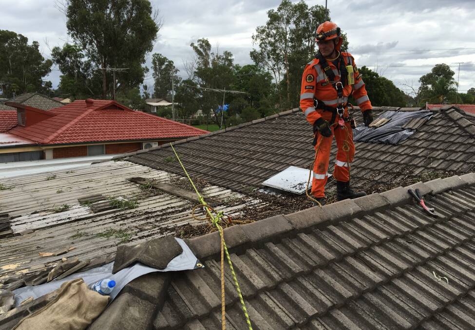 Lloyd Jones of Moruya SES works to repair a roof, damaged from a fallen tree, at Mount Druitt, Sydney, on the weekend.