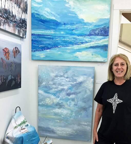 Featured artist: Mel Reidy wearing one of her own handprinted T-shirts in front of her paintings, 'Sky Reflection' (top) and 'Sky's Magic Touch'.