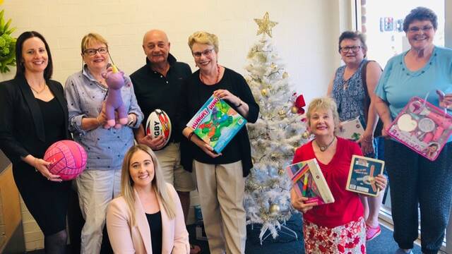 Gifts for kids: Christmas elves from Uniting Church and St Vincent de Paul gather with Ray White staff around the tree in the Ray White office, Batehaven.