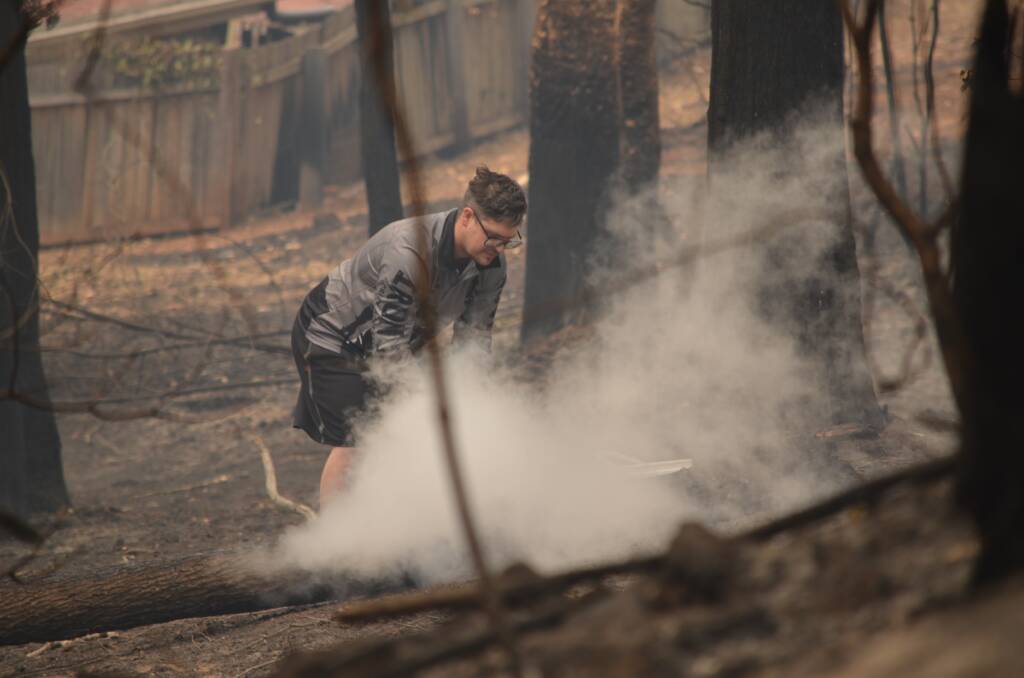A man enters urban no man's land, extinguishing smouldering bush between Heron Road and Penguin Place, Catalina on New Year's Day, January 1.