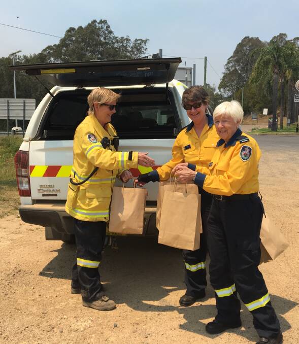 A Eurobodalla Shire RFS member receives food parcels at Nelligen from Eurobodalla Catering Brigade senior deputy captain Jen Pearson and deputy captain Trin Taber. 